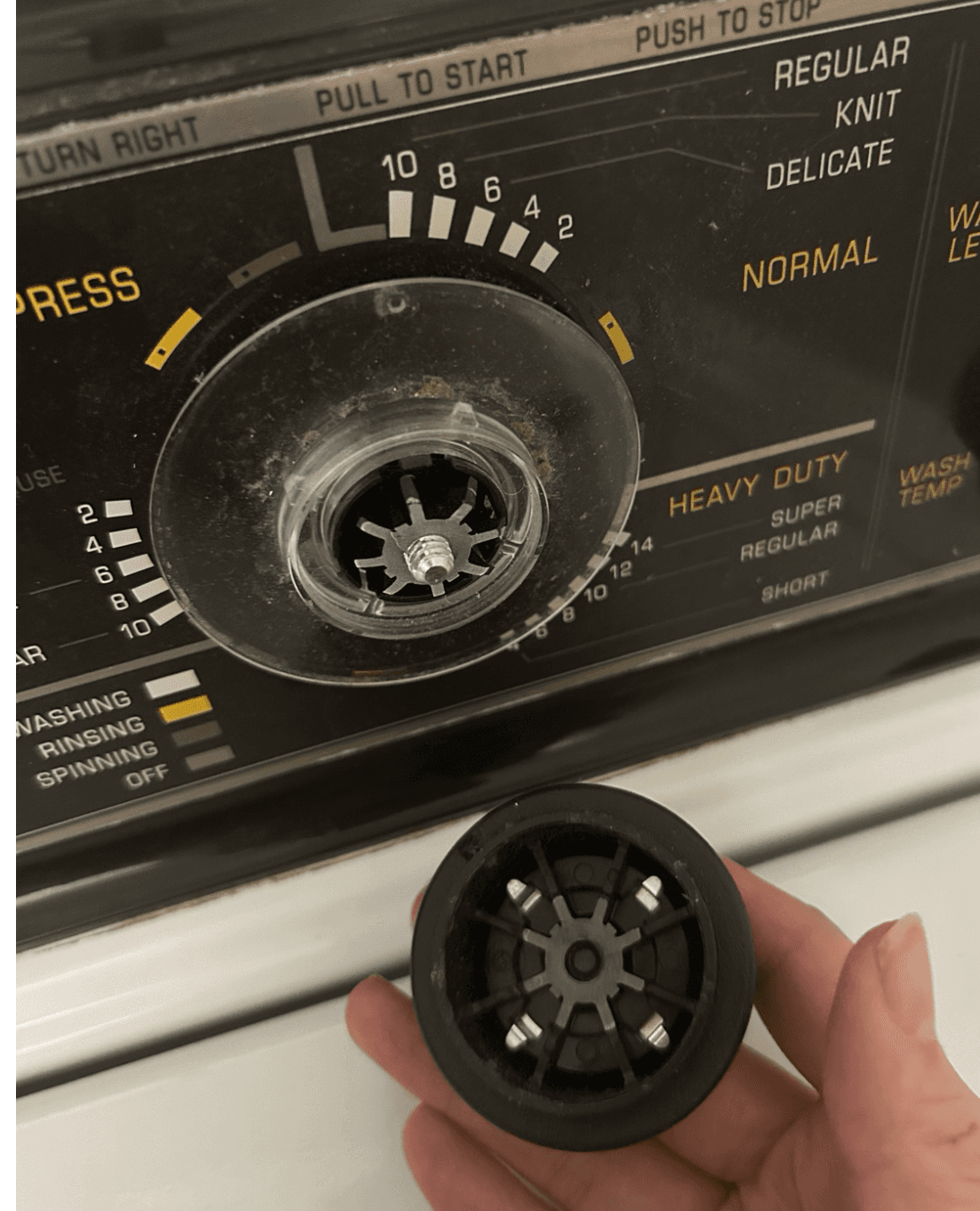 Washing-machine timer dial with an exposed central shaft and a detached black control knob held below it.